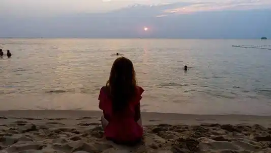 坐在海滩上,美丽的日落景色,瑜伽概念,在平静的海浪中观看大海照片