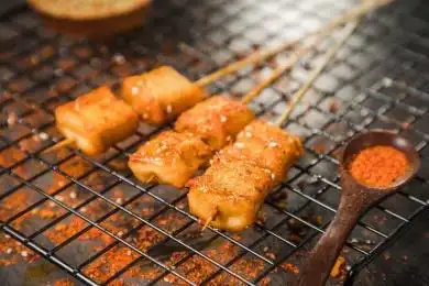 黑色烤架上放着几串撒着辣椒面油炸鱼豆腐