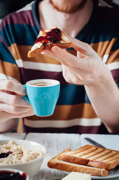 吃面包加黄油和果酱休息的胡子的年轻人