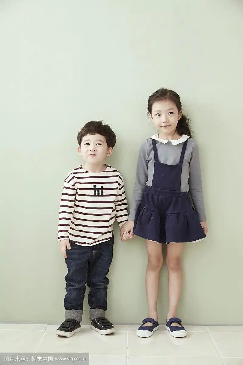 小男孩和小女孩手牵着手站在墙前的照片