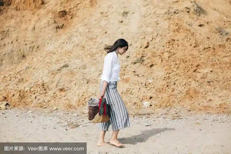时髦的时髦女孩赤脚走在沙滩上,手里拿着包和鞋.