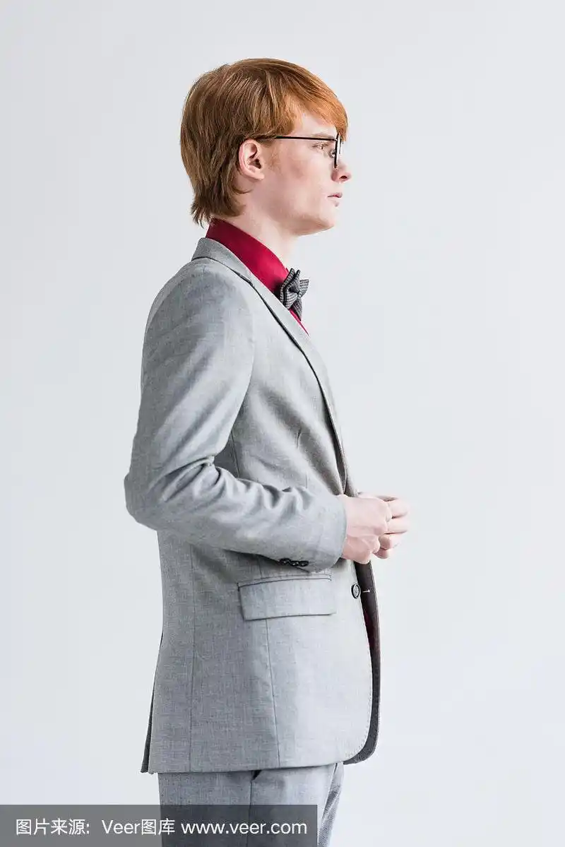 侧面的男时装模特在眼镜穿着西装孤立在灰色