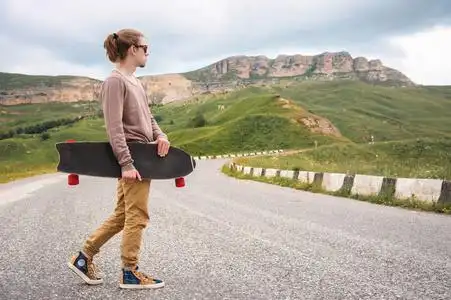 的傍晚,一个时髦的年轻人手里拿着溜冰鞋或长木板沿着蜿蜒的山路行走