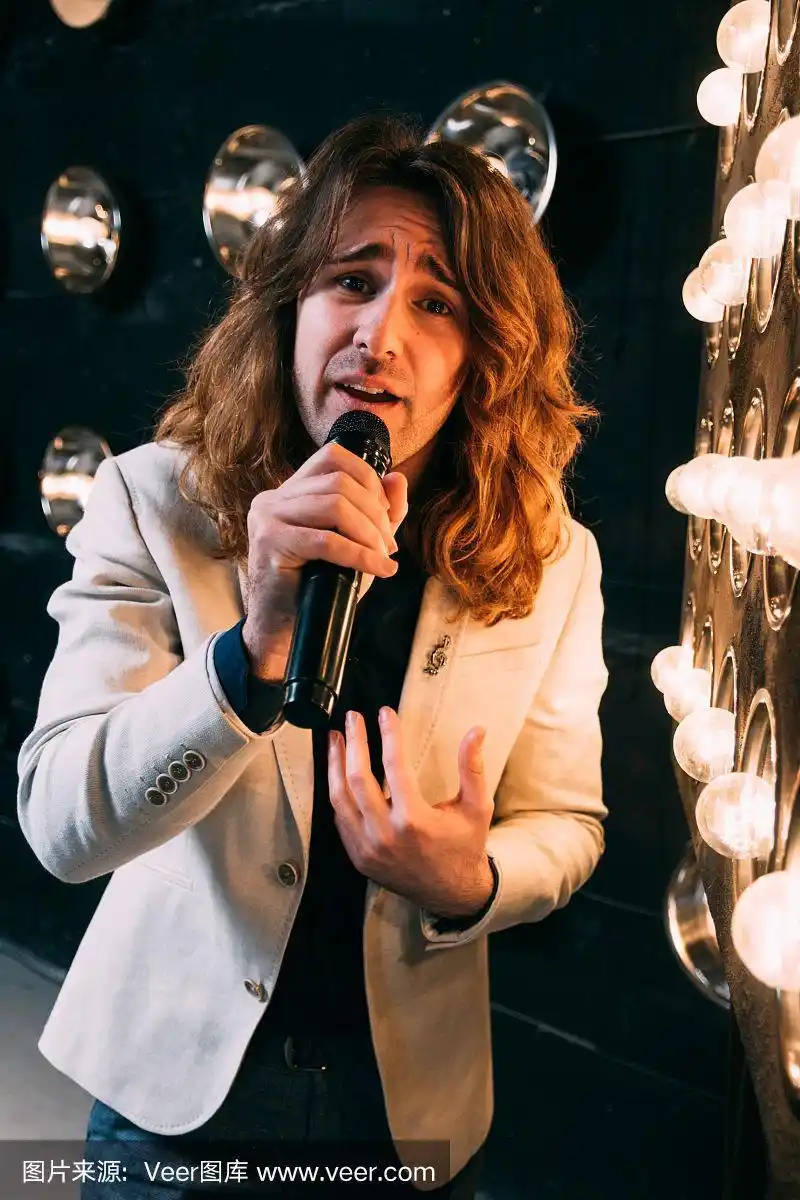 男歌手留着长发,拿着麦克风站在舞台上
