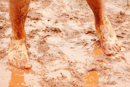 男人的赤脚脚在泥泞的水坑里