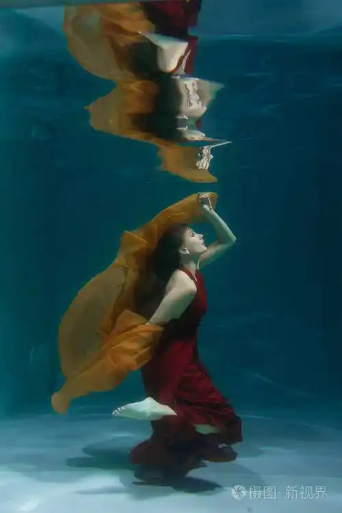 美丽个美丽的自由潜水员一个人穿着红色的长裙独自在深水中游泳