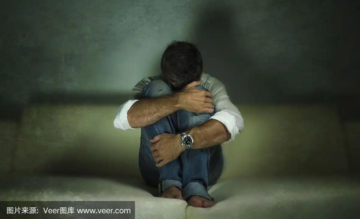 男人在家里的沙发上哭泣,在痛苦和绝望中遭受焦虑危机和抑郁问题上