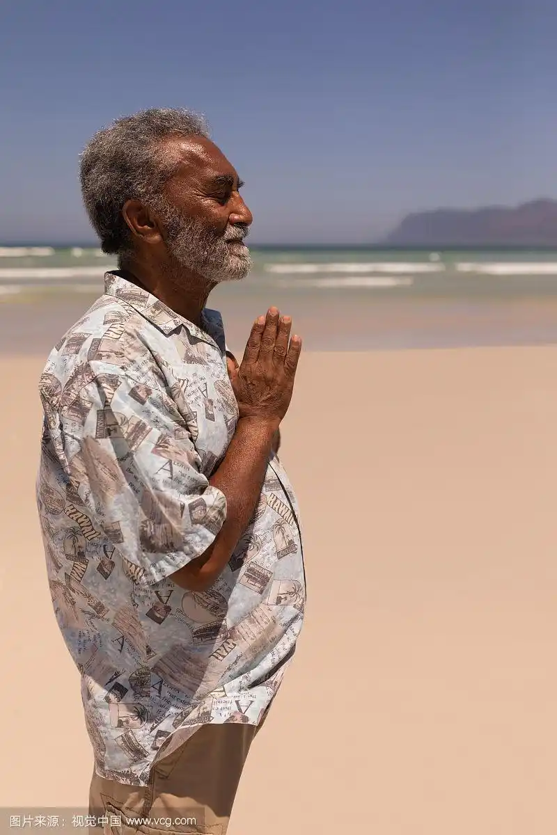 在海滩上双手合十祈祷的黑人老人