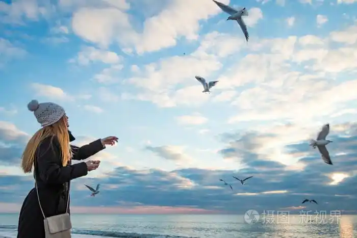 戴着白色的针织帽,在蓝天的映衬下,喂养着海滩上的海鸥