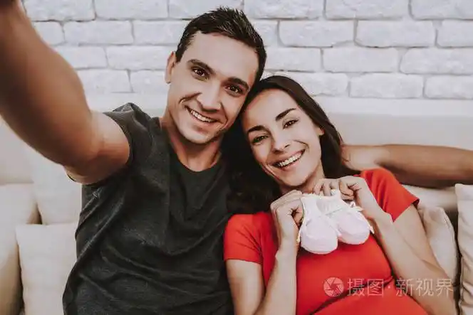 情侣正在手机上自拍. 夫妻是男人和孕妇. 女孩拿着一双童鞋.