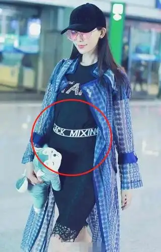 照片中林志玲现身机场,手里抱着一只玩具熊用来遮住肚子,然而身穿