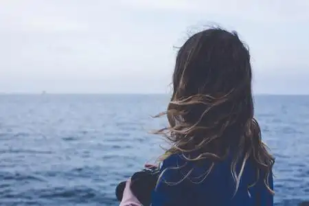 卷曲女孩在看着朦胧的阳光透过厚厚的雾平静的大海和蓝天的背影照片