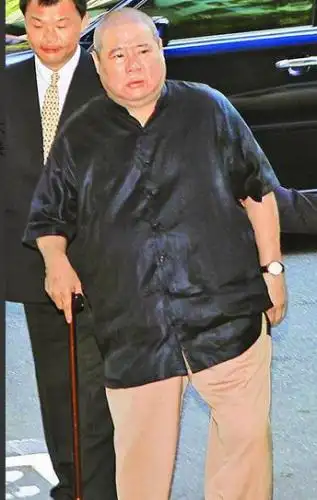 "竹联帮"老大黄少岑拄着手杖,缓缓步入追思会现场,身边有多名黑衣人