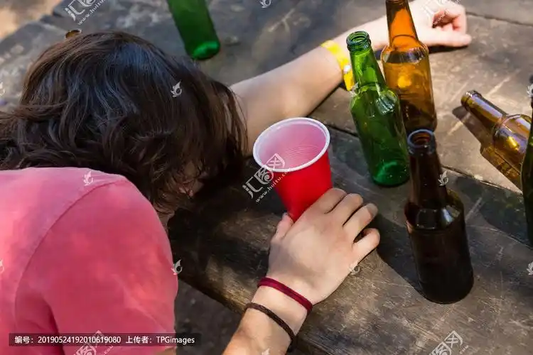 在公园里,一个醉汉靠在桌子上拿着一个玻璃杯.