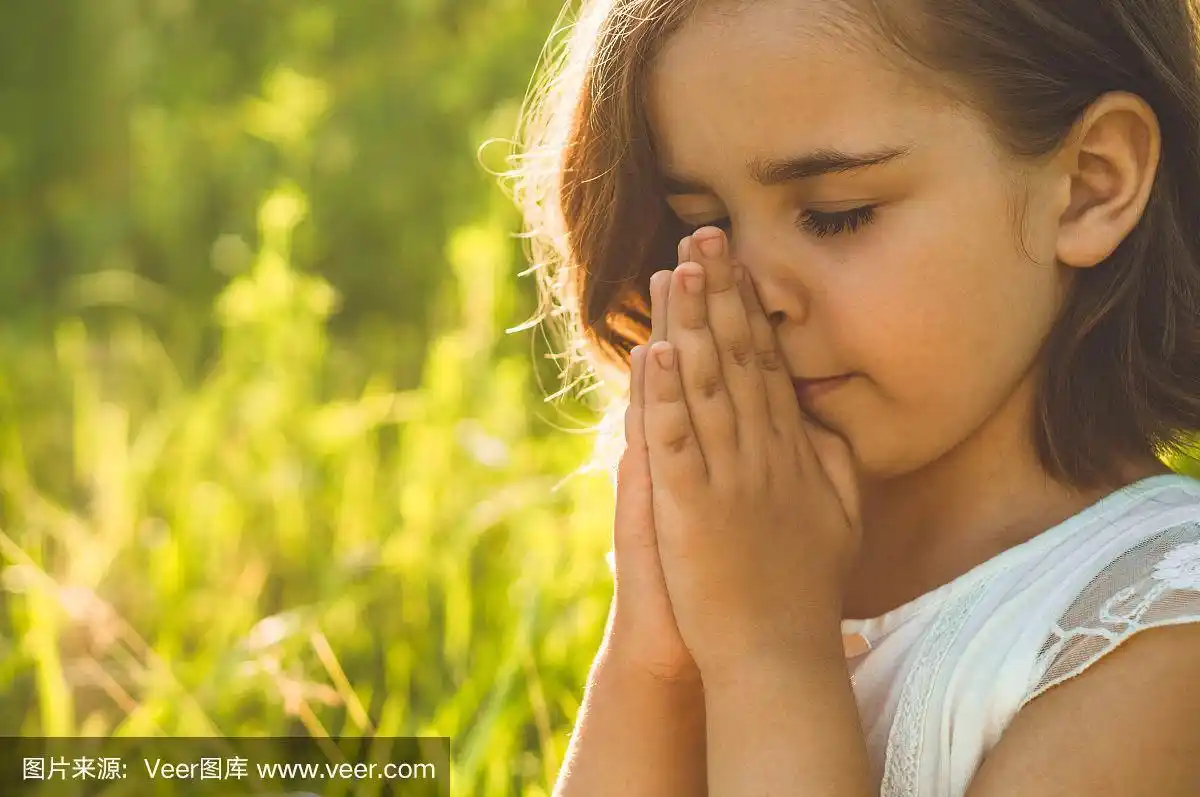 在美丽的日落时分,小女孩闭上眼睛,在田野里祈祷.
