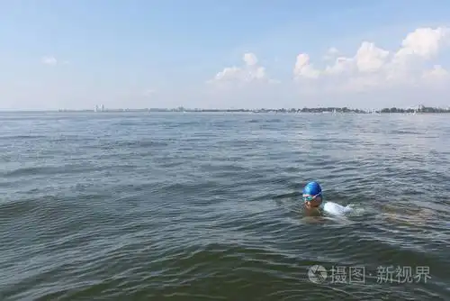 年轻人在一个蓝色的帽子和护目镜河里游泳