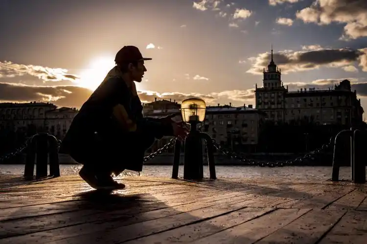 日落时蹲在水边的男子的侧影.
