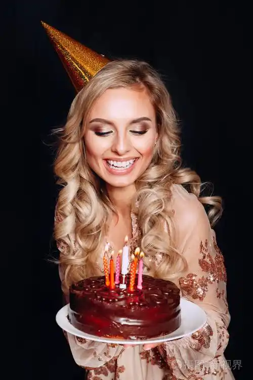 一个年轻美丽的金发女孩拿着生日蛋糕与蜡烛在黑色背景的肖像