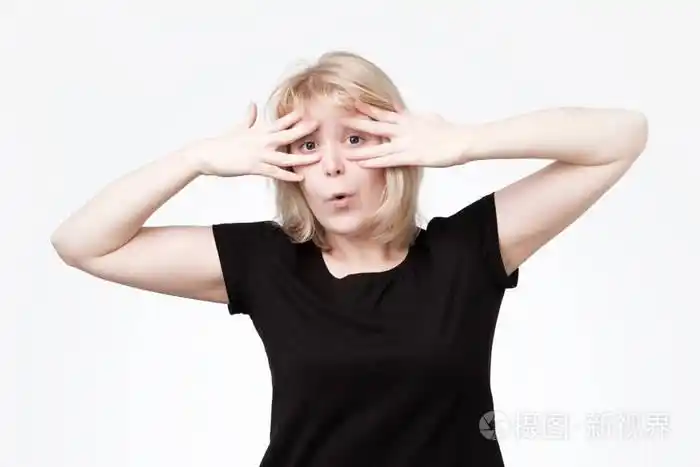 害羞的胆小少女用双手捂住脸, 通过手指偷看镜头