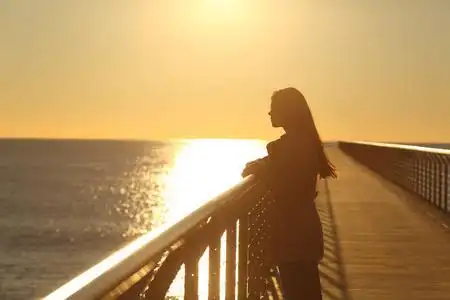 日落时分,一个女人独自从一座桥上眺望大海女人瑜伽大海和岩石旁的