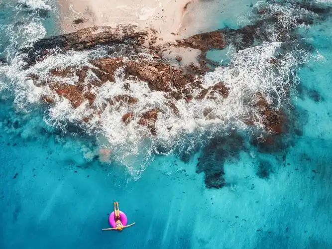 年轻女子在马尔代夫透明的绿松石海的粉红色游泳环上游泳的鸟瞰图.