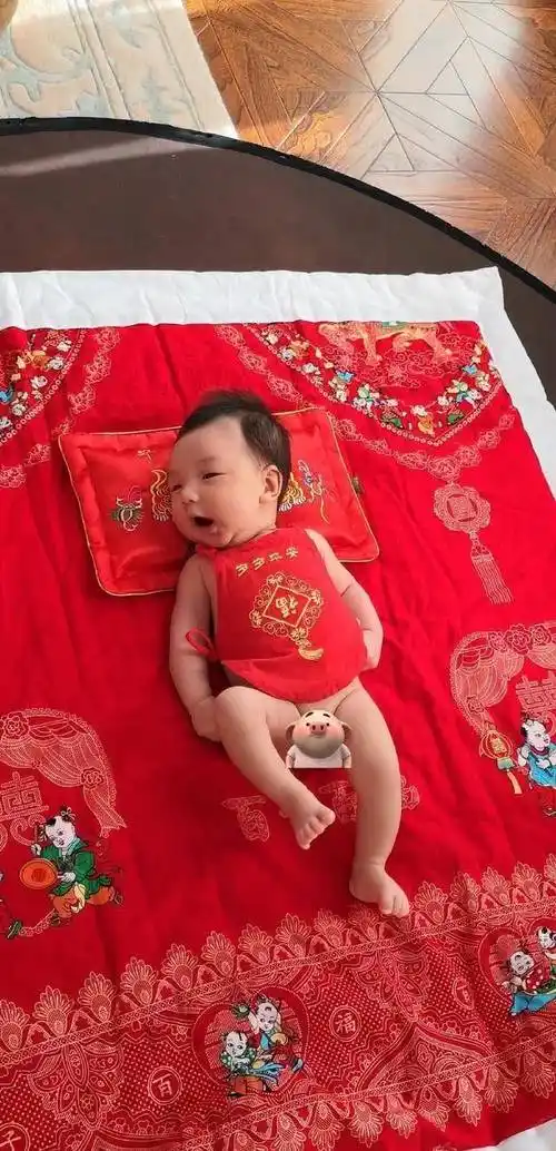 照片当中,王二妮的儿子穿着一身红色的时尚躺在非常喜庆的红色床单