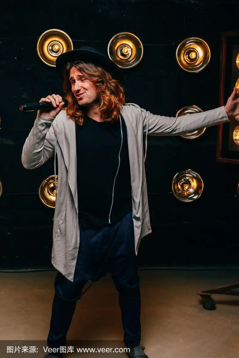 男歌手留着长发,拿着麦克风站在舞台上