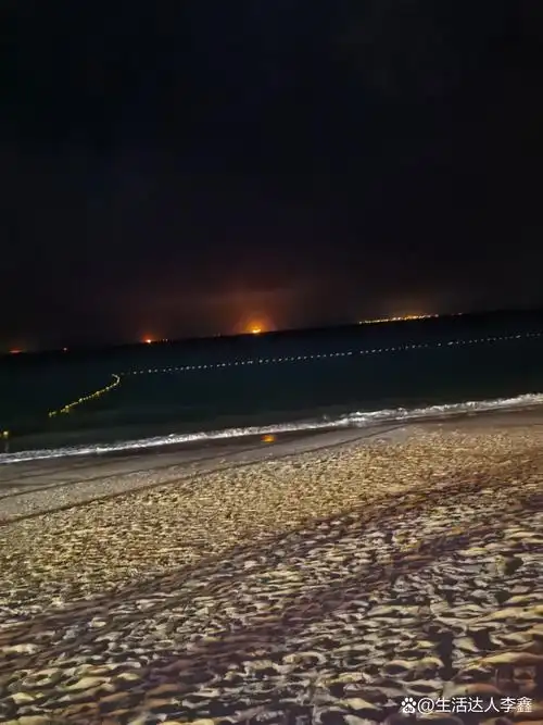 夜晚的海边,沙滩上留下一串脚印,远处城市灯光闪烁.#治愈系风景
