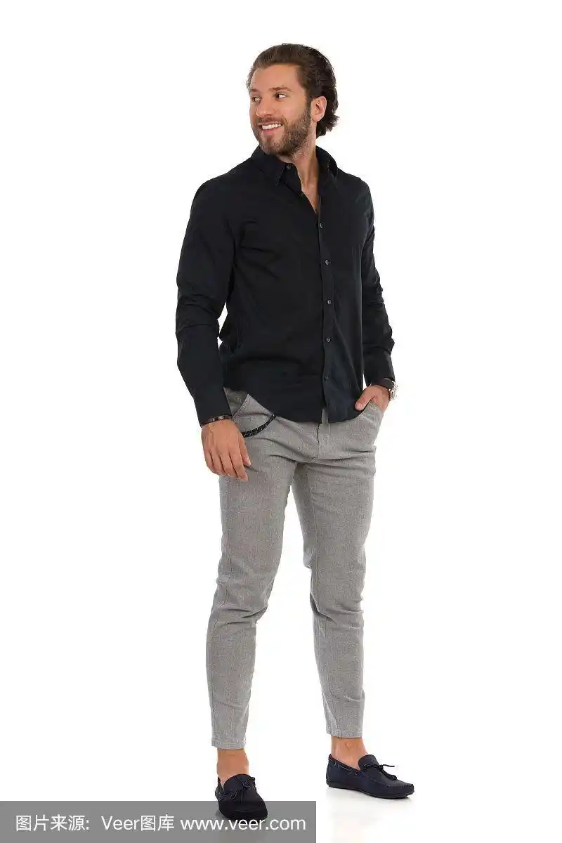 穿着灰色裤子,鹿皮鞋和黑色衬衫的英俊男子站在那里看向别处