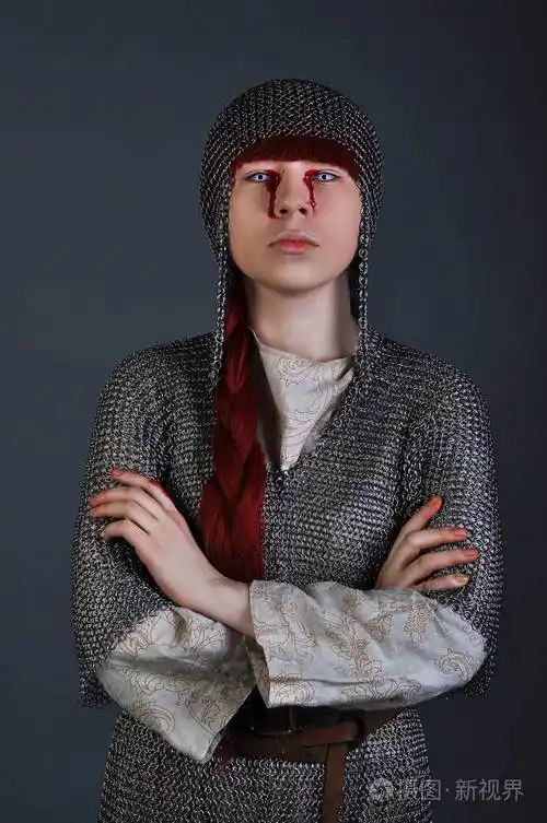 中世纪女孩在链邮件与红色的头发站在灰色的背景, 她的手上的血