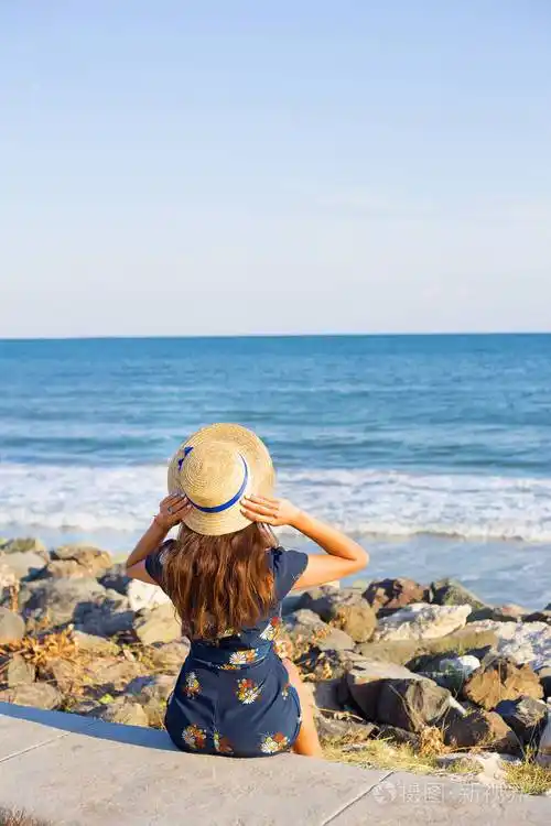 美丽的女孩在一顶帽子在海边坐在石头上