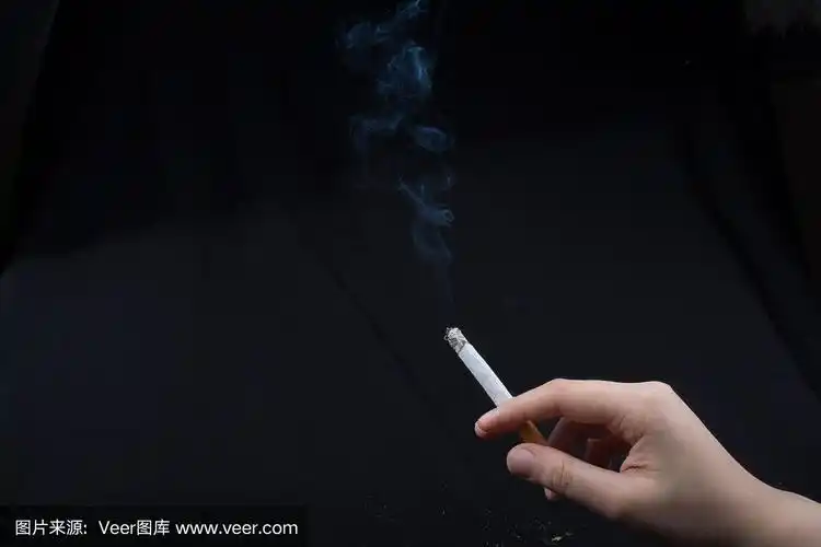在黑色的背景下,手握着正在吸烟的香烟