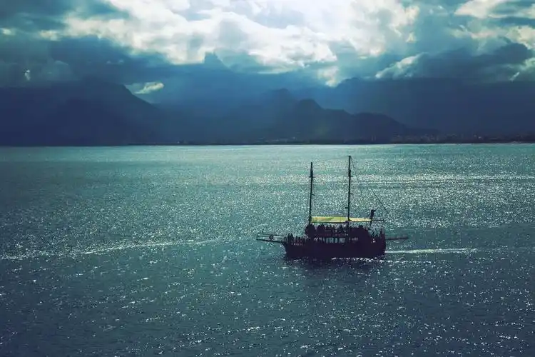 一艘帆船在多云的天空下靠近群山航行