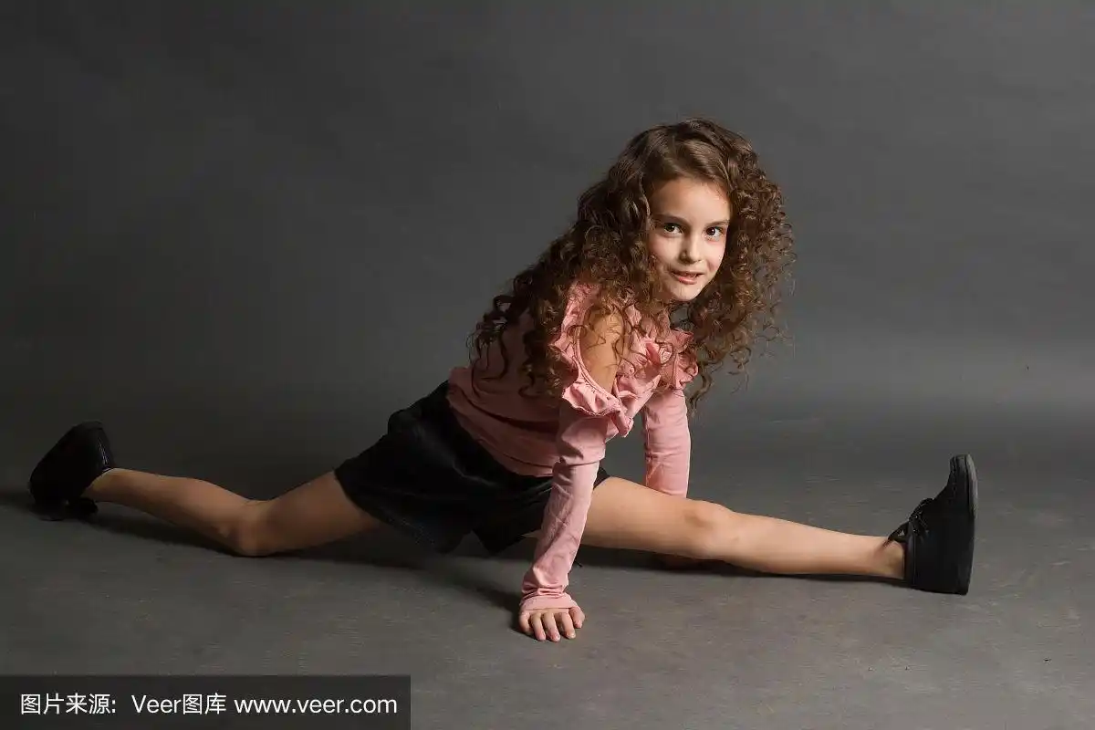小女孩穿着粉色衬衫和紧灰色背景坐在劈叉