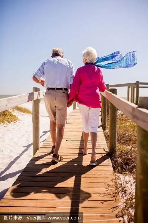 一对退休的老夫妇手牵着手在海滩上散步