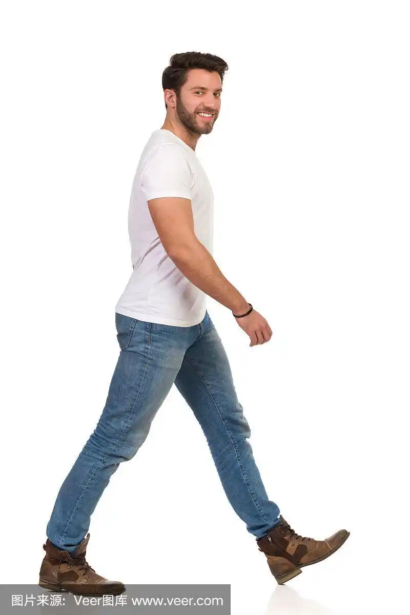 穿着牛仔裤和白色t恤的年轻人正在走路,看着相机的侧视图