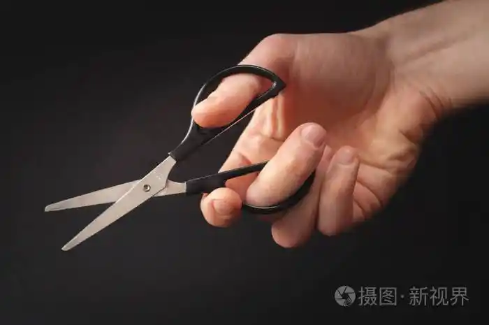 男手拿着一把小剪刀在黑色背景上的照片手