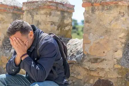 悲伤夹克一个悲伤的男人,穿着夹克,背着背包,手放在脸上,坐着照片