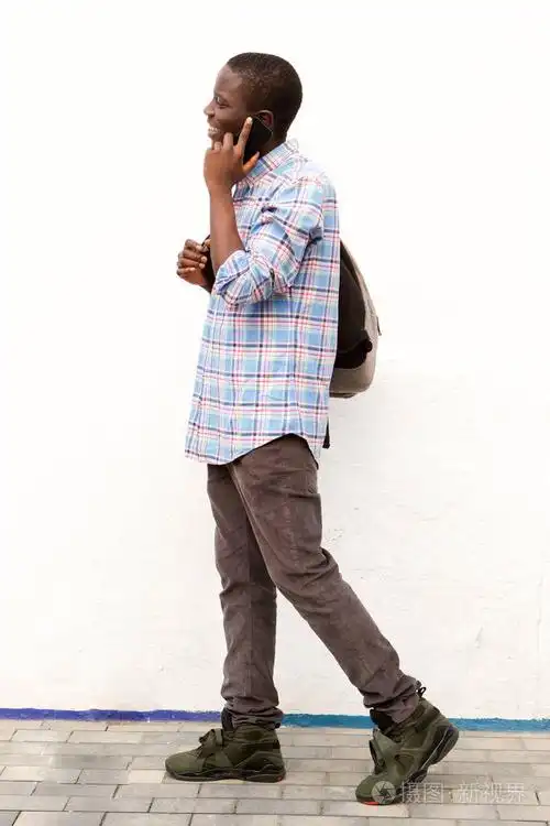 非洲年轻人全身侧面的肖像走在外面与袋子和手机
