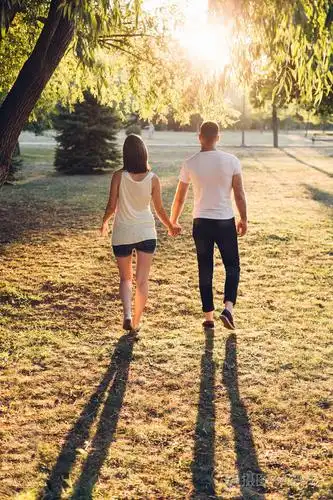 丈夫的后景,怀孕的妻子牵着手,在晴天在公园散步