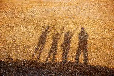 一家四口在淡黄色沙砾上的背光倾斜影子