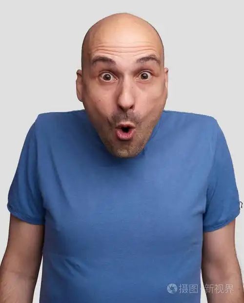 英俊的秃头男子肖像在蓝色t恤看着镜头与凸起的眉毛和惊讶的脸表情