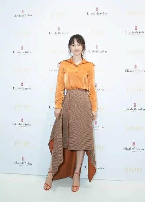 白百何身穿橘色衬衣,下穿褐色格纹不规则伞裙,脚踩橘色一字带凉鞋