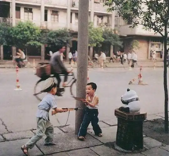 80年代中国儿童历史老照片:图为两个小男孩拿着两把玩具冲锋枪在街边