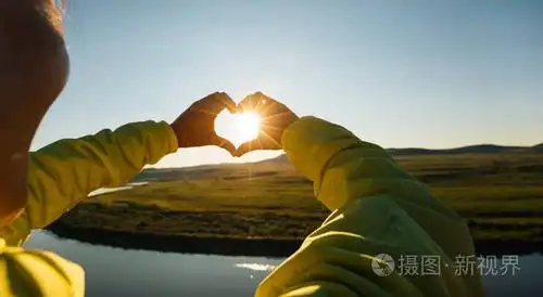 人类的手,在落日的天空作心形手势