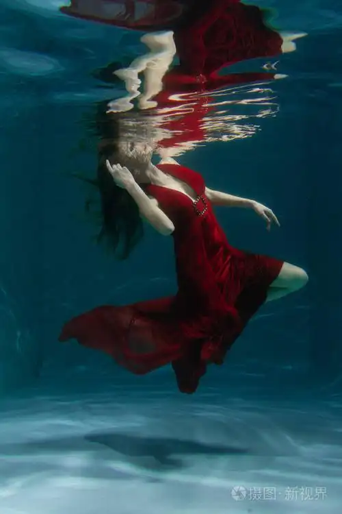一个美丽的自由潜水员,一个人穿着红色的长裙,独自在深水中游泳照片