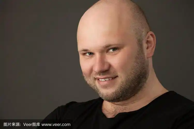 一名35岁剃着光头的大胡子男子的工作室肖像,他穿着黑色t恤,背景是