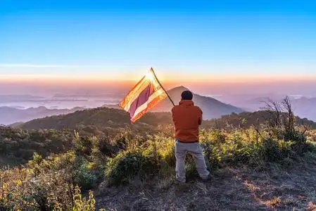 穿着的年轻人的背部观看坐在莲花在山顶享受惊险的风景高绿色的山在徒