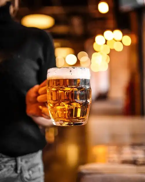 模糊背景中一个女人手里端着一杯啤酒手拿着杯子淡啤酒模糊的暖灯