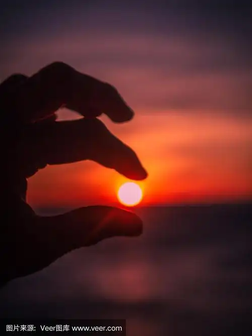 一只手在海边,手指间握着夕阳